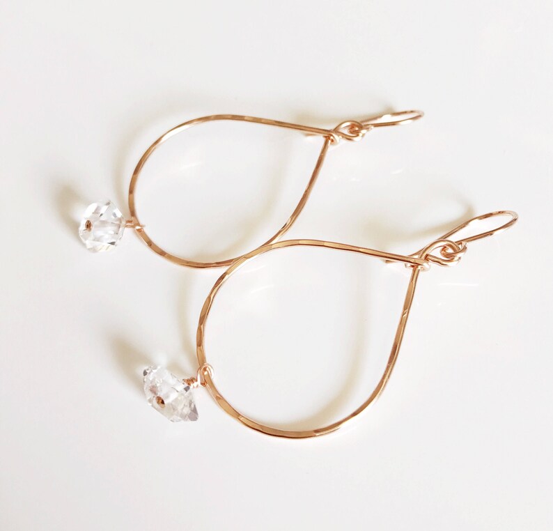 May include: Rose gold teardrop earrings with clear crystal accents. The earrings are made of hammered metal and have a delicate, feminine look.