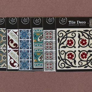 Könnte beinhalten: Sechs Packungen Tile Deco Fliesenaufkleber von Beija Flor. Jede Packung zeigt verschiedene Muster, darunter florale, geometrische und geschwungene Motive in den Farben Blau, Rot, Schwarz, Creme und Petrol. Das Markenlogo ist abgebildet.