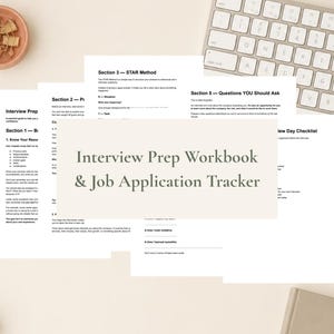May include: A printed Interview Prep Workbook & Job Application Tracker with multiple pages featuring sections on the STAR method, interview preparation, and a checklist, displayed with a white computer keyboard and gold paper clips nearby.