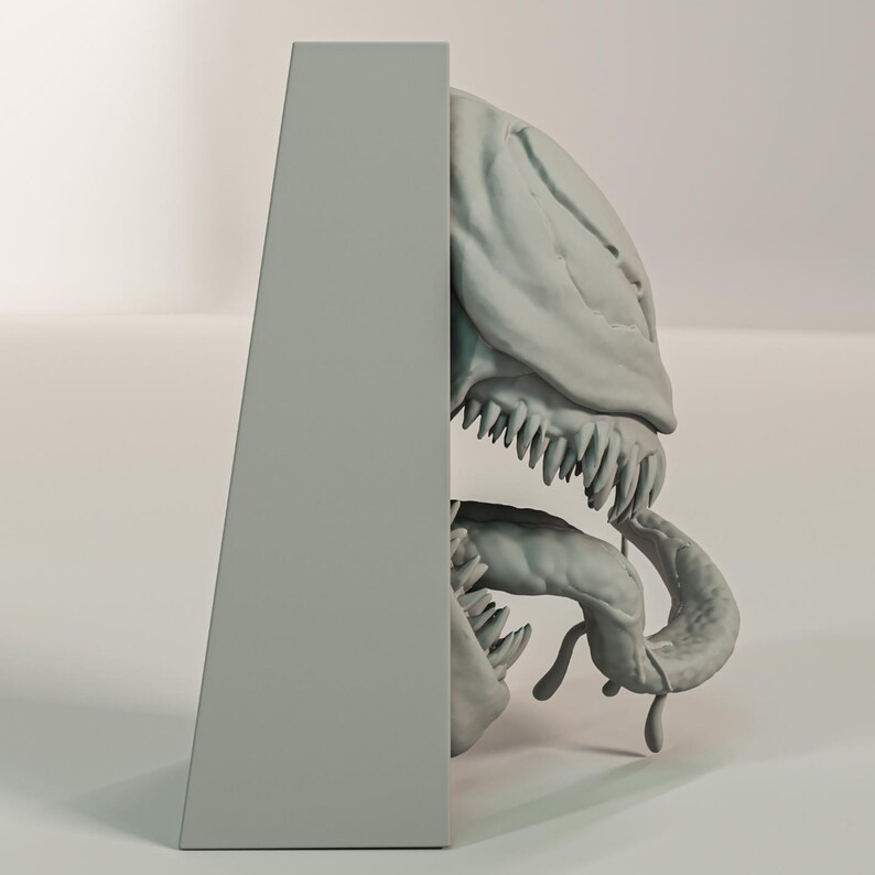 Pu&ograve; includere: Una scultura grigia stilizzata di un cranio e di una mascella di creatura, con denti affilati e una lingua curva. La scultura &egrave; parzialmente nascosta da un supporto rettangolare grigio.