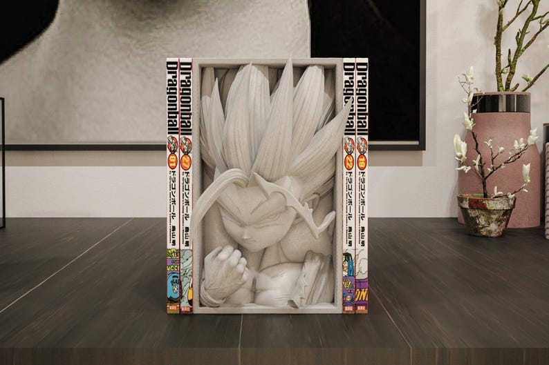 Puede incluir: Escultura blanca de un personaje de Dragonball Z con pelo puntiagudo, enmarcada por dos vol&uacute;menes del manga Dragonball. Las lomos del manga son visibles, con texto japon&eacute;s e ilustraciones coloridas. La escultura est&aacute; sobre una superficie oscura.