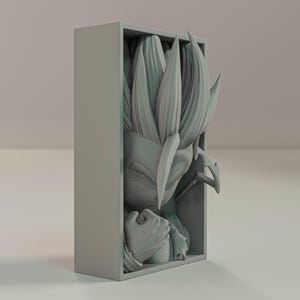 Puede incluir: Escultura gris impresa en 3D de un personaje con pelo puntiagudo y expresi&oacute;n decidida, dentro de un marco rectangular. El pu&ntilde;o cerrado y los rasgos faciales detallados de la figura son prominentes. Una obra de arte coleccionable.