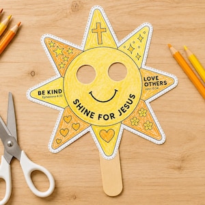 May include: A yellow sun-shaped paper mask with a smiley face, attached to a wooden craft stick. The mask features the text SHINE FOR JESUS, BE KIND Ephesians 4:32, and LOVE OTHERS John 13:34, along with drawings of stars, hearts, flowers, and a cross.