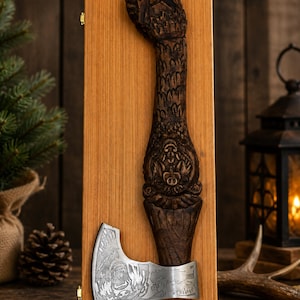 May include: A handcrafted axe with a detailed, carved wooden handle mounted on a wooden plaque. The axe head is silver-colored with an engraved design. The handle is dark brown with intricate carvings. The axe is displayed against a rustic wooden background.