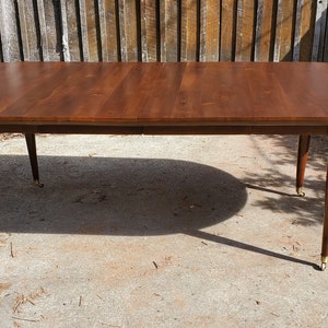 May include: A vintage oval-shaped wooden dining table with a dark brown finish. The table has four tapered legs with brass feet and a smooth, polished surface.