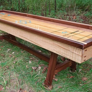 May include: A wooden shuffleboard table with a walnut stained frame and a maple playing surface. The table has a traditional design with a center line and scoring areas.