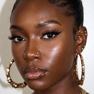 May include: Large gold bamboo-style hoop earrings paired with a layered gold chain necklace. The jewelry features a polished metallic finish, with the circular hoops showcasing a textured, segmented bamboo design and the necklace consisting of linked chains.