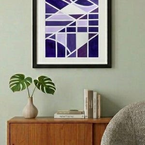 May include: Abstract geometric art print in a black frame. The artwork features a design of intersecting lines and shapes in shades of purple and white. The print is displayed above a wooden cabinet.