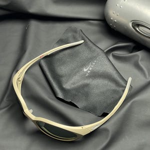 Puede incluir: Gafas de sol color beige con lentes oscuras y un estuche a juego. Las gafas de sol est&aacute;n sobre un pa&ntilde;o de microfibra negro con el nombre de la marca impreso. Dise&ntilde;o elegante y deportivo.