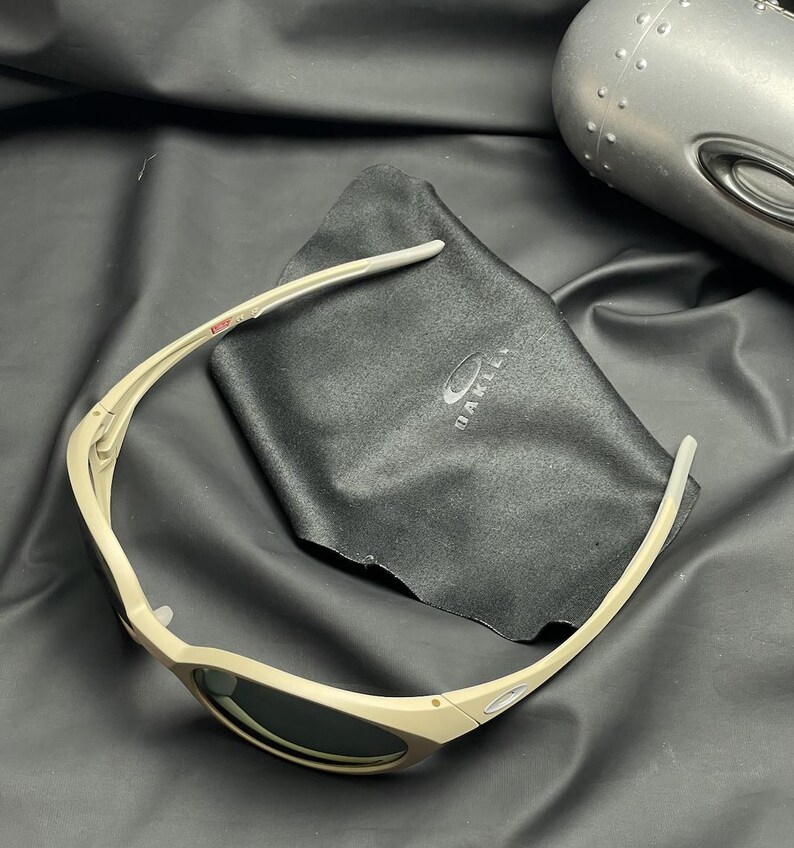 Puede incluir: Gafas de sol color beige con lentes oscuras y un estuche a juego. Las gafas de sol est&aacute;n sobre un pa&ntilde;o de microfibra negro con el nombre de la marca impreso. Dise&ntilde;o elegante y deportivo.