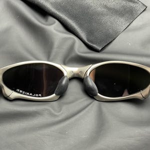 May include: Silver-framed sunglasses with dark lenses and black nose pads. The word "POLARIZED" is printed on the left lens. A black microfiber cleaning cloth is in the background.