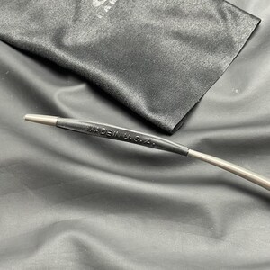 May include: Close-up of an eyeglass arm with the text "MADE IN U.S.A." printed on a black rubber sleeve. The arm is silver and extends from the sleeve. A black microfiber cloth is in the background.