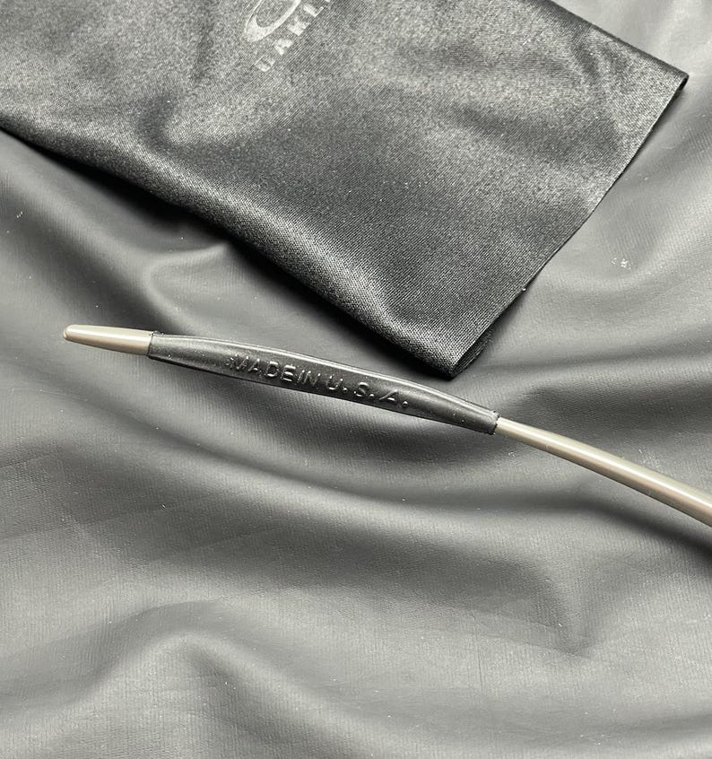 May include: Close-up of an eyeglass arm with the text "MADE IN U.S.A." printed on a black rubber sleeve. The arm is silver and extends from the sleeve. A black microfiber cloth is in the background.