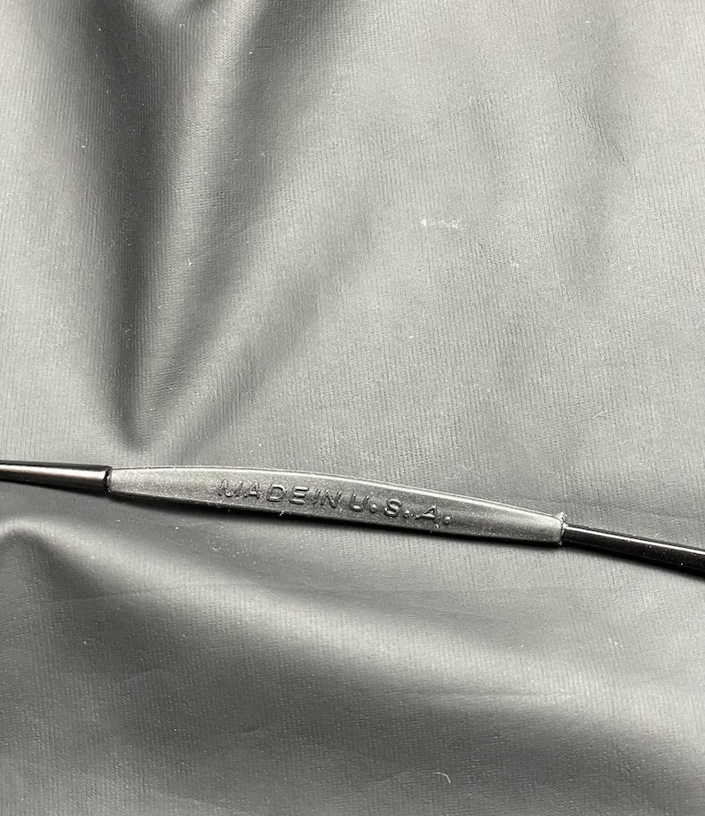 May include: Close-up of a black eyeglass frame with the text "MADE IN U.S.A." printed on the bridge. The frame is made of a matte black material.