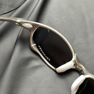 May include: Silver-framed sunglasses with black polarized lenses. The sunglasses have white nose pads and the word "POLARIZED" is printed on the lens. The frame is a metallic silver color.