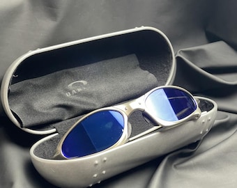 Gafas de sol vintage Oakley Penny Titanium Ice con estuche rígido y lentes azules. Estilo vintage de los 90 para ciclismo, running, estilo gorpcore y actividades al aire libre.