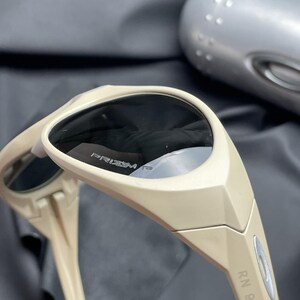 Puede incluir: Gafas de sol beige con lentes oscuras. Las gafas de sol tienen un dise&ntilde;o deportivo con el texto "PRIZM" visible en la lente. La montura es de color beige claro y las patillas tienen el texto "RN 96".