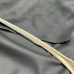 Puede incluir: Primer plano de unas gafas de sol beige y blancas. El texto "eye jacket" est&aacute; impreso en la patilla. Las gafas est&aacute;n sobre una tela gris oscura.