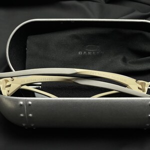 Puede incluir: Gafas de sol beige y grises con el texto "PIET TACTICAL FIELD GEAR" y "RN 96548-CA35460" impreso en la montura. Las gafas de sol est&aacute;n dentro de un estuche plateado con interior negro y un pa&ntilde;o negro.
