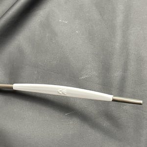 May include: A close-up of a medical instrument with a white handle and dark gray metal ends. The handle has the letters "CE" printed on it. The instrument is on a dark gray surface.
