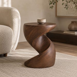 May include: A dark brown wooden side table featuring a distinct spiral or hourglass-shaped base with a smooth, circular top surface. A small, neutral-toned ceramic bowl sits centred on the flat top of the table, showcasing visible wood grain.