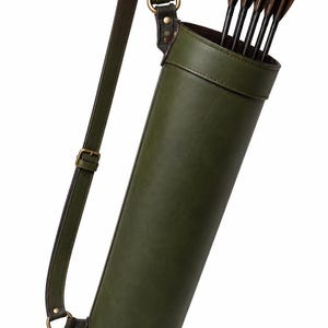 May include: A cylindrical olive green quiver with a matching adjustable shoulder strap featuring brass-toned metal hardware. The quiver contains five black arrows with dark brown fletching, held securely by a reinforced top rim and side attachments.