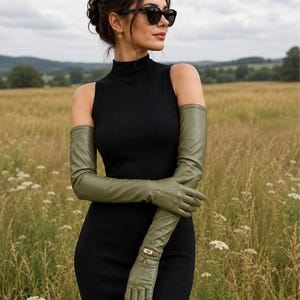 Peut inclure: Une paire de gants longs en cuir vert olive, dotés d'une bride à boucle dorée au niveau du poignet. Ces gants montent au-dessus du coude et sont fabriqués en cuir lisse avec des coutures apparentes le long des doigts et de la paume.
