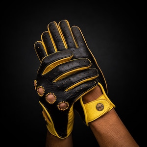 Puede incluir: Guantes de conducción de cuero negro y amarillo con detalles perforados. Los guantes tienen detalles amarillos en los dedos, la muñeca y las costuras. La muñeca presenta un emblema circular. Los guantes están diseñados para conducir y ofrecen un aspecto elegante.