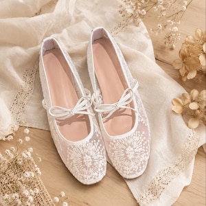 Könnte beinhalten: Ein Paar weiße Ballerinas aus transparentem Netzstoff mit aufwendiger weißer Blumenstickerei an den abgerundeten Zehenkappen. Jeder Schuh verfügt über eine zarte weiße Schleife aus Band auf der Oberseite und einen schlichten weißen Rand.