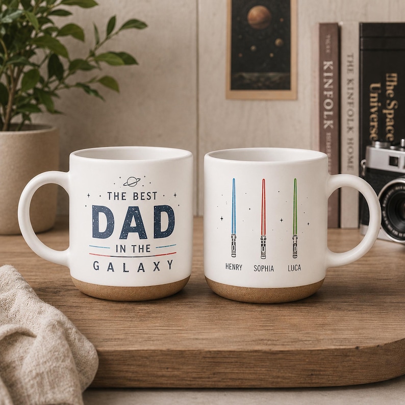 May include: Two white ceramic mugs with a speckled brown base. One mug features the text THE BEST DAD IN THE GALAXY with a small planet icon. The other mug displays three vertical lightsabers in blue, red, and green with the names HENRY, SOPHIA, and LUCA.