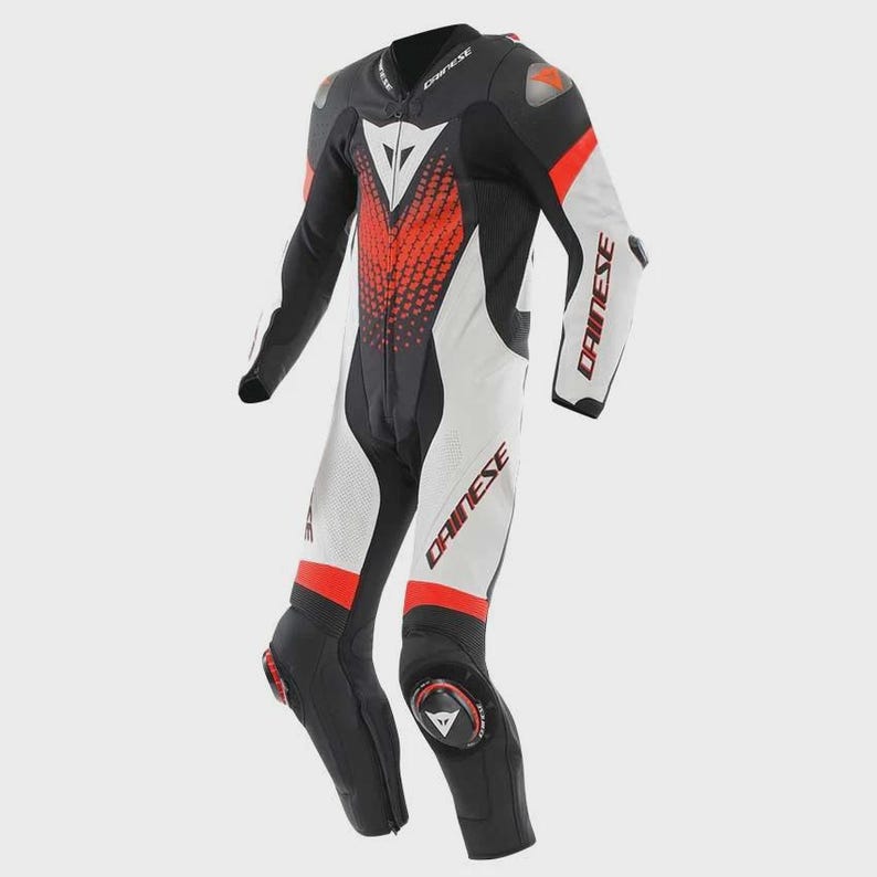 May include: A Dainese motorcycle racing suit in black, white, and red. The suit features a central zip, protective shoulder and knee sliders, and the Dainese logo printed on the chest, sleeves, and legs. It has a textured red pattern on the chest.