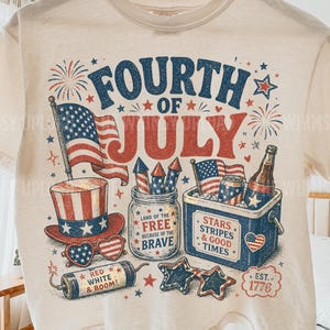 May include: Cream-colored t-shirt with a Fourth of July graphic. The design features patriotic imagery including an American flag, fireworks, a hat, sunglasses, and a cooler with drinks. Text includes "Fourth of July", "Land of the Free", and "Stars, Stripes & Good Times".