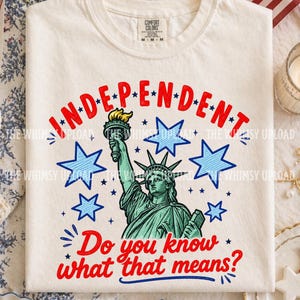 May include: Cream-colored t-shirt featuring the Statue of Liberty and the word "INDEPENDENT" in red, with blue stars. The phrase "Do you know what that means?" is also in red. The shirt has a crew neck and a Comfort Colors tag.