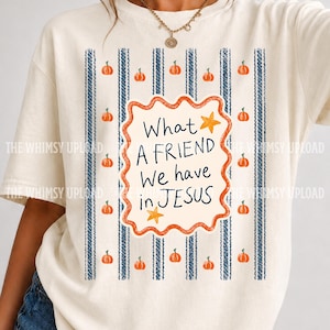 Op de afbeelding: Een crèmekleurig T-shirt met korte mouwen en een centrale afbeelding met een geschulpte rand, de tekst "What A FRIEND We have in JESUS" en twee gele sterren. Het achtergrondpatroon bestaat uit verticale blauwe gestructureerde strepen en oranje pompoenen.