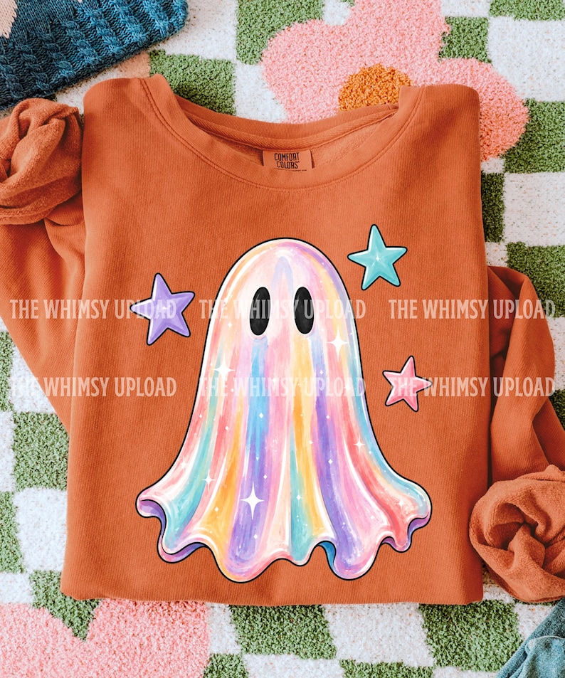 May include: An orange crewneck sweatshirt featuring a central graphic of a ghost with a multi-colored iridescent finish. The ghost is surrounded by three small stars in light blue, purple, and pink. The inner neck label reads Comfort Colors.