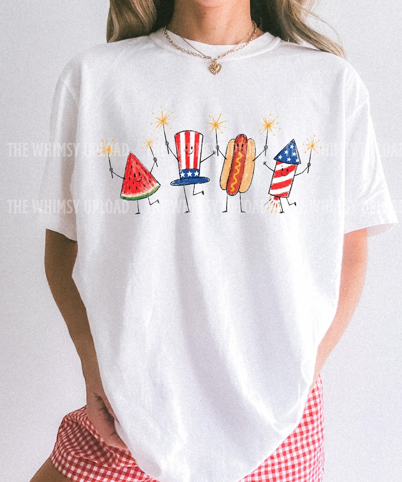 May include: White t-shirt featuring a whimsical illustration of a watermelon slice, a hot dog, a firework, and a patriotic hat, each holding sparklers. The design is in red, white, and blue, perfect for Independence Day celebrations.