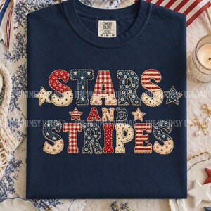 May include: Navy blue t-shirt with the words "STARS AND STRIPES" in a patchwork design. The letters are in red, white, and blue patterns, including stars, stripes, and gingham. A patriotic themed tee.