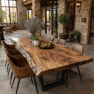 Peut inclure: Une grande table à manger rectangulaire avec un plateau en bois massif à bord naturel présentant des motifs de grain et des nœuds, soutenue par des pieds en U en métal noir, entourée de six chaises en cuir marron avec des pieds en métal noir.