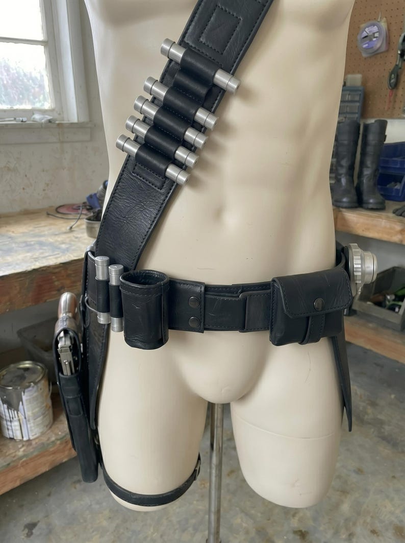 May include: Black leather utility belt with silver-tipped cartridge holders, a holster, and pouches. The belt is displayed on a mannequin. The belt includes a thigh strap and a shoulder strap.