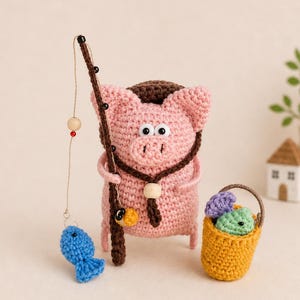 May include: A crocheted pink pig figurine with a fishing rod and a blue fish. The pig wears a brown hat and necklace. A yellow basket contains crocheted fish. The scene is set against a light background.