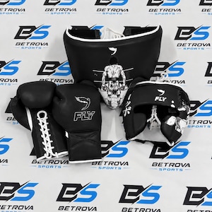 Könnte beinhalten: Ein schwarzes Boxset bestehend aus einem Paar Schnür-Boxhandschuhen, einem Kopfschutz und einem Tiefschutz. Jedes Teil ist mit weißen grafischen Illustrationen eines Boxers und dem Text FLY verziert. Die Ausrüstung hat weiße Schnürsenkel und Ränder.