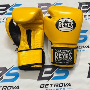 Peut inclure: Une paire de gants de boxe jaune vif avec des bordures noires et une doublure intérieure noire. Les gants présentent le logo Cleto Reyes en noir et blanc sur la sangle du poignet et le dos de la main, avec le texte Hecho en Mexico Professional.