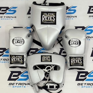 Peut inclure: Un ensemble d'équipement de boxe argenté comprenant deux gants de boxe, une coquille de protection et un casque. Chaque article comporte un écusson noir et blanc avec le logo Cleto Reyes et le texte Cleto Reyes Hecho en Mexico Profesional.