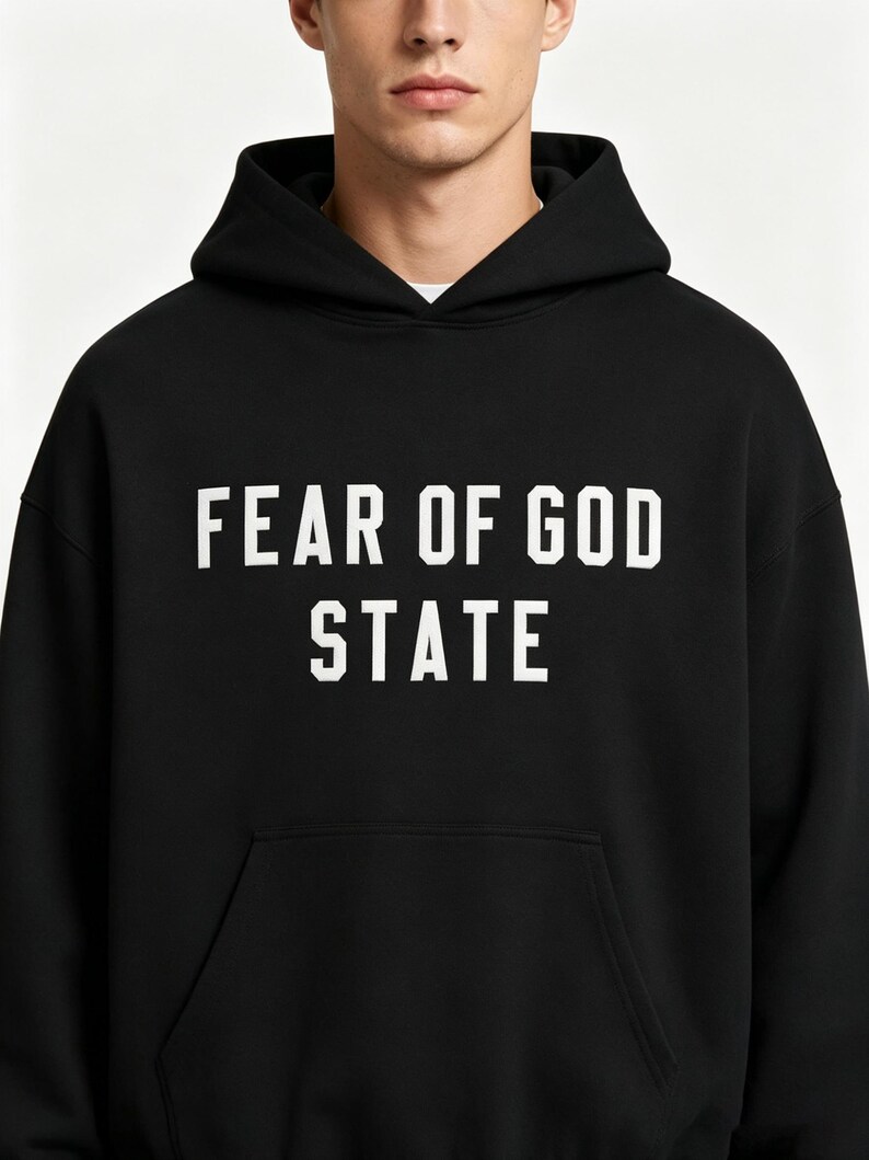May include: Black hoodie with the text "FEAR OF GOD STATE" in white block letters. The hoodie has a front pocket and a hood. The person in the image is wearing a white undershirt.