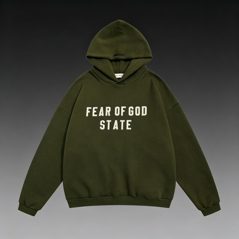 May include: An olive green hoodie with the text "FEAR OF GOD STATE" in white block letters across the chest. The hoodie has a drawstring hood and long sleeves. The background is a gradient of dark gray and black.