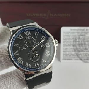 Puede incluir: Un reloj de lujo Ulysse Nardin Le Locle con esfera negra, bisel plateado y correa de caucho negra. El reloj presenta n&uacute;meros romanos y m&uacute;ltiples subesferas. Fabricado en Suiza.