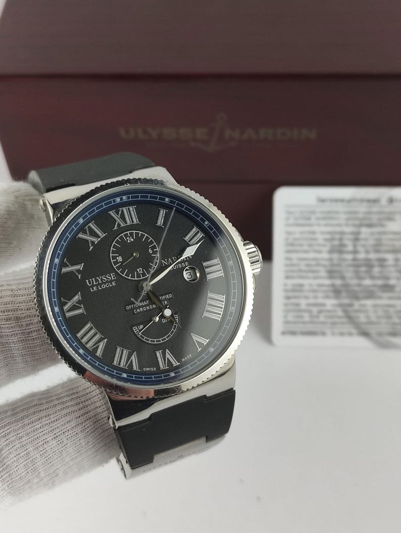 Puede incluir: Un reloj de lujo Ulysse Nardin Le Locle con esfera negra, bisel plateado y correa de caucho negra. El reloj presenta n&uacute;meros romanos y m&uacute;ltiples subesferas. Fabricado en Suiza.