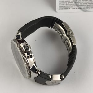 Puede incluir: Un reloj de pulsera de lujo con una correa de goma negra y una caja de acero inoxidable plateada. El reloj presenta una esfera negra y un bisel texturizado. El reloj est&aacute; dise&ntilde;ado para la durabilidad y el estilo.