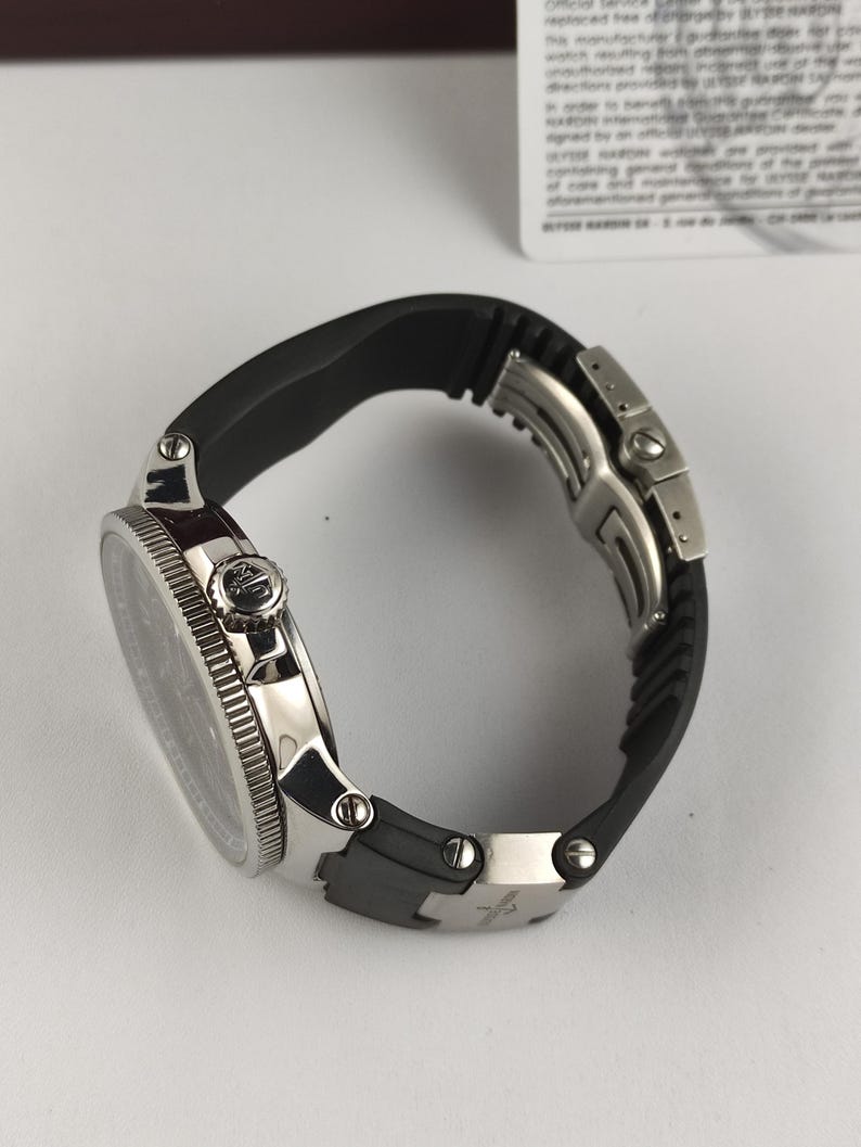 Puede incluir: Un reloj de pulsera de lujo con una correa de goma negra y una caja de acero inoxidable plateada. El reloj presenta una esfera negra y un bisel texturizado. El reloj est&aacute; dise&ntilde;ado para la durabilidad y el estilo.