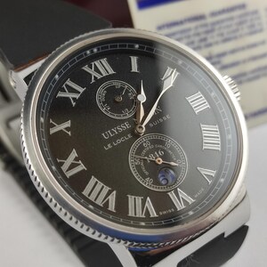 K&ouml;nnte beinhalten: Nahaufnahme einer Luxus-Armbanduhr mit schwarzem Zifferblatt und silbernem Geh&auml;use. Die Uhr hat r&ouml;mische Ziffern und zwei Hilfszifferbl&auml;tter. Sie hat ein schwarzes Lederarmband. Der Markenname "ULYSSE NARDIN" ist sichtbar.